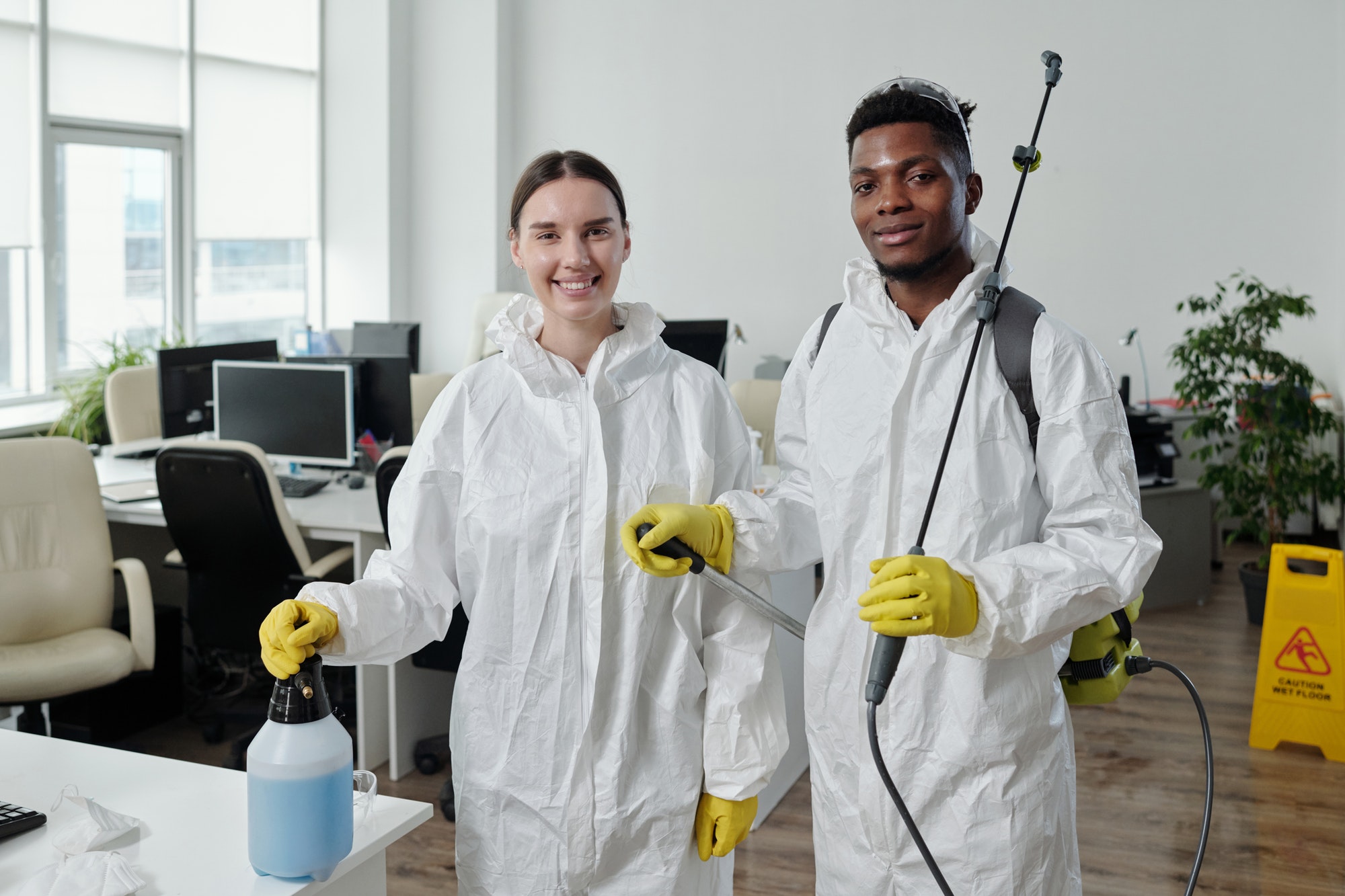 Two happy young workers of cleaning service in protective overalls and gloves